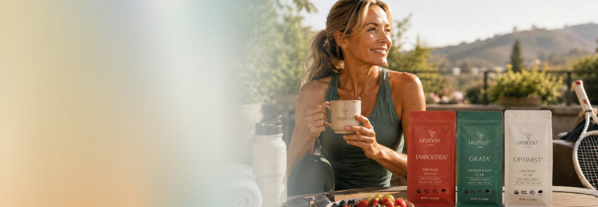 Woman holding coffee beside Lifeboost coffee bags after an outdoor workout.
